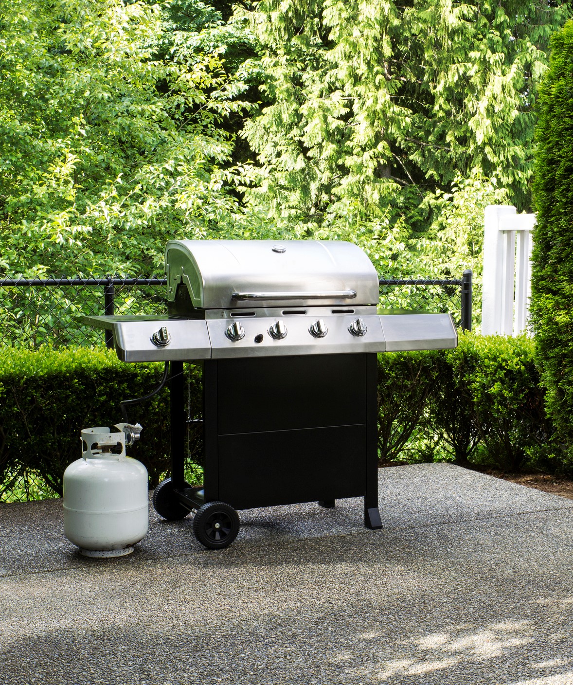 Horizontal photo of a large barbeque cooker on concrete outdoor patio with woods and deck in background